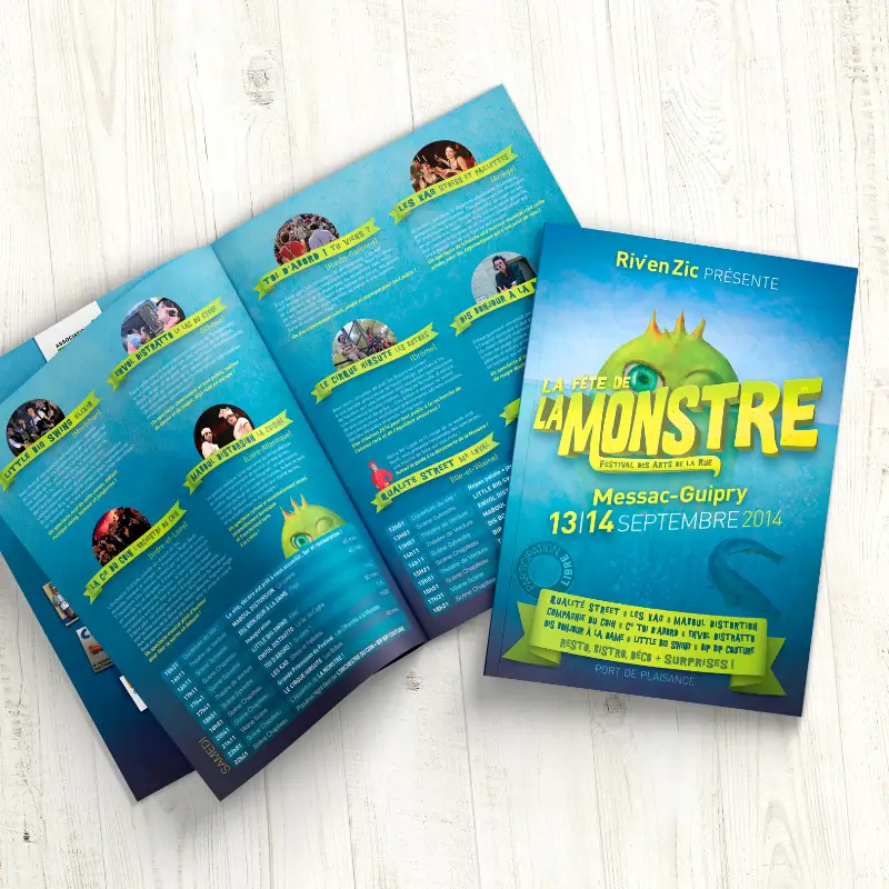 Couverture et pages intérieures dépliées du programme bleu du festival La Monstre sur fond en bois clair